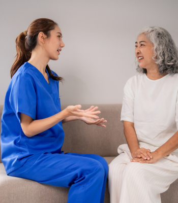A caregiver attentively listening to an older client in her living room.