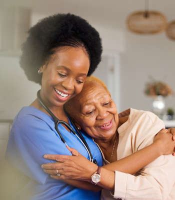 EverCare nurse hugging an older woman in a bright kitchen during a home visit.